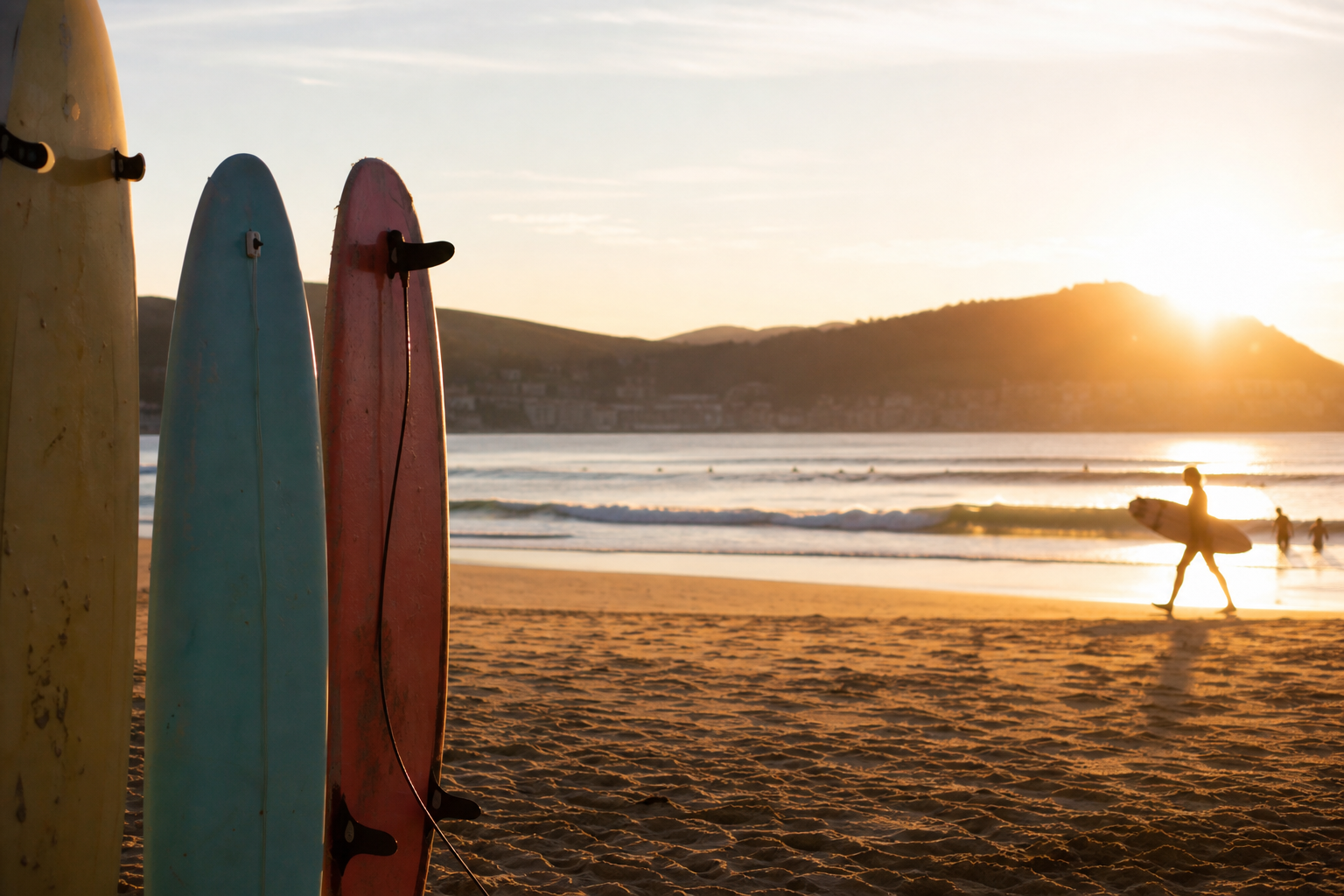 Playa de Zarautz al atardecer con tablas de surf clavadas en la arena y olas suaves rompiendo